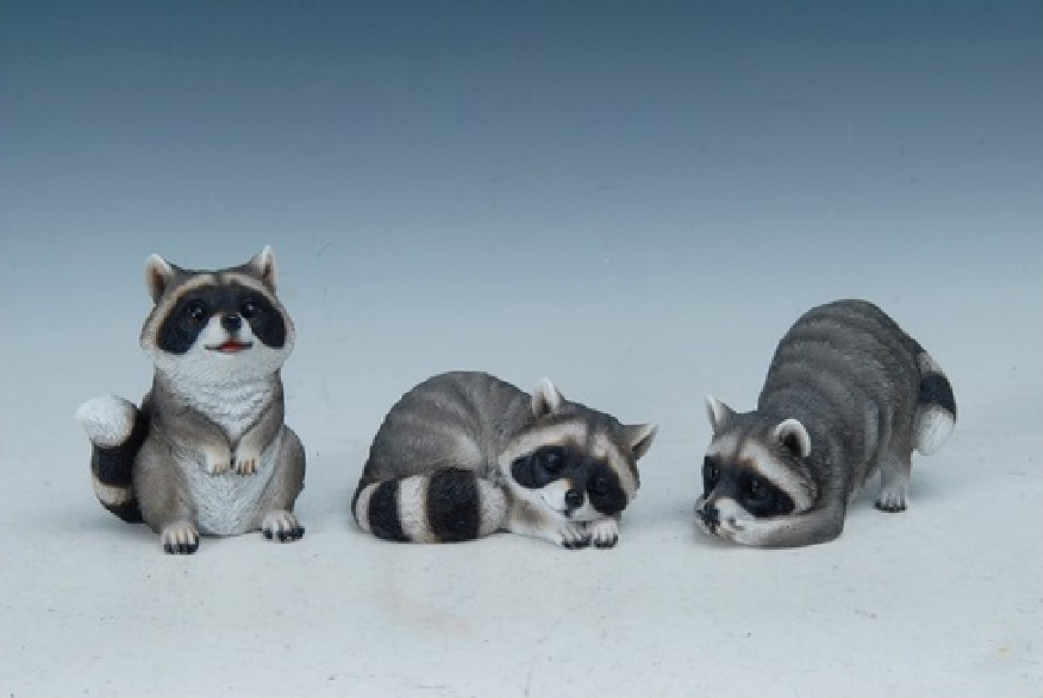 Three raccoon figurines on a white background.  One sitting up, one laying down, one leaning down with head on front paws.