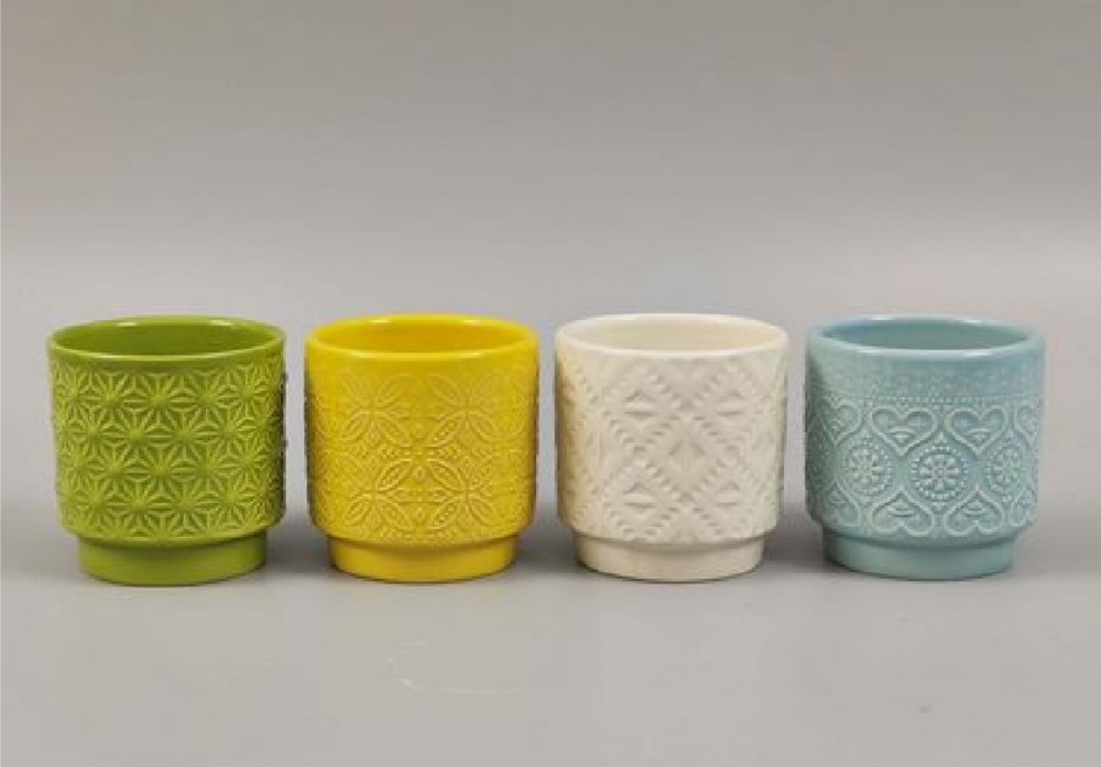 Four textured ceramic cups in green, yellow, white, and blue on a gray background