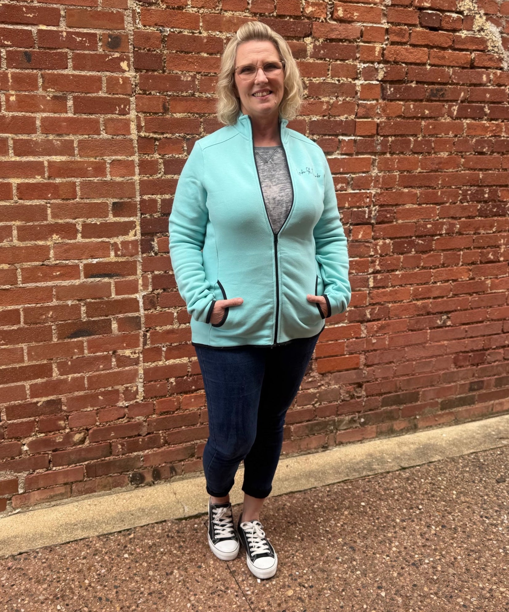 Woman wearing a light blue jacket standing against a brick wall.